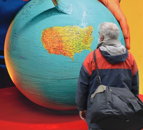a man stands in front of a picture that is a large globe with everything painted light blue except the USA