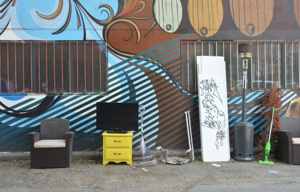 cast off furniture in a lane, two chairs, a TV, a small yellow set of drawers, a mop, 