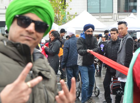 a man in a green turban is close in the foreground and is out of focus. He is wearing sunglasses and is giving the peace sign with both hands