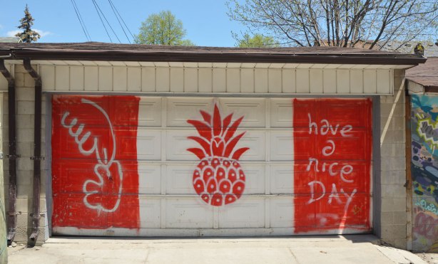 On a gararge door in a laneway, painted like the Canadian flag except there is a pineapple in the middle instead of a maple leaf. On the right hand side red stripe are the words "have a nice day"