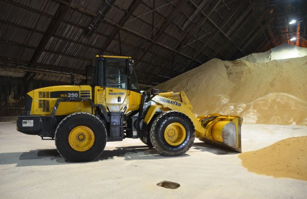 a large yellow front end loaded is parked inside a warehouse. A large pile of raw sugar is in the background. 