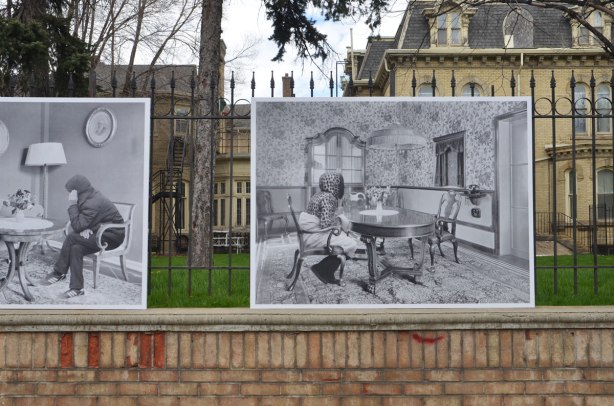 photos mounted along the exterior of a wrought iron fence around the Italian Consulate, right beside the sidewalk. The consulate is on old brick house (mansion) from the 1800's - the photos are of refugees that have been photoshopped into old photos of the interior of the apartment of a wealthy person from the 1920's