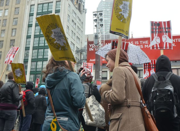 women talking and laughing together at a rally, holding placards that say "Build a Solidarity City"
