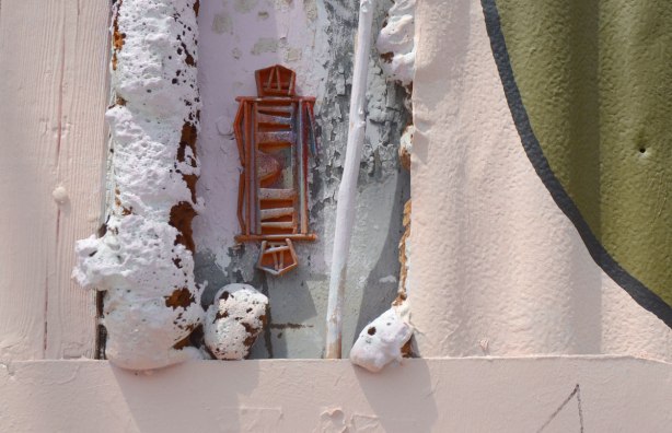 orange coloured stikman, double, foot to foot, in a pink wall with foam insulation on both sides of him