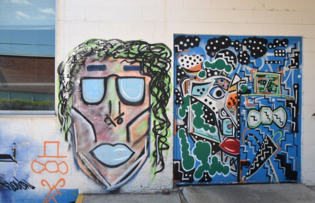 A door covered with a very abstract face painting and another graffiti face beside the door. 