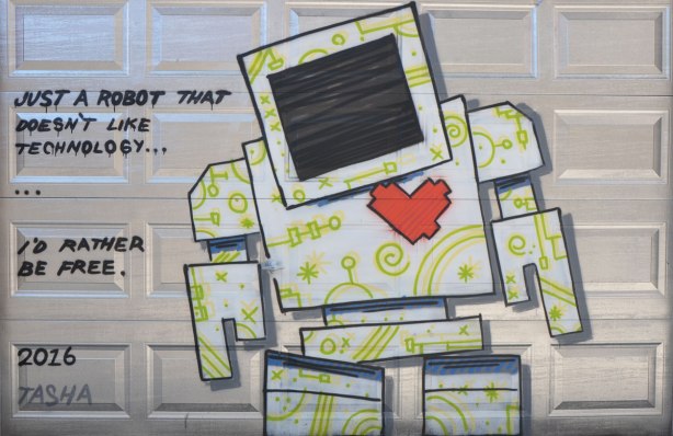 a lovebot on a silver garage door with the words "Just a robot that doesn't like technology, I'd rather be free"- signed Tasha