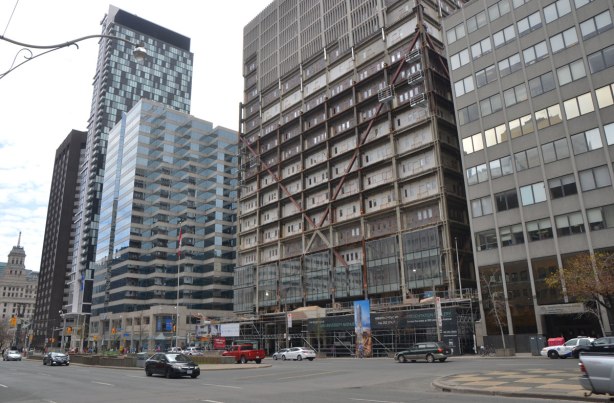 Tall office building is having its concrete facade replaced with glass. The upper floors are still concrete, the middle floors are bare and the lower floors have new glass 