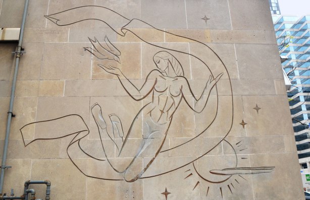 outline drawing of a woman floating in the sky, incised into limestone facade of a building. She is releasing a bird.