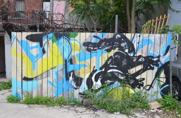 a wood fence with a graffiti painting of a black alligator or crocodile on it. in an alley