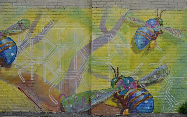 part of a large mural on a wall in a lane, three very big bees