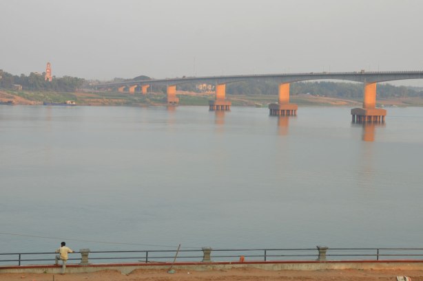 a man stands beside a river, bridge in the background, Mekong River