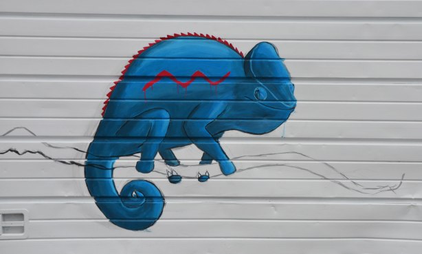 graffiti street art animals painted on garage door in an alleyway - a bright blue chameleon