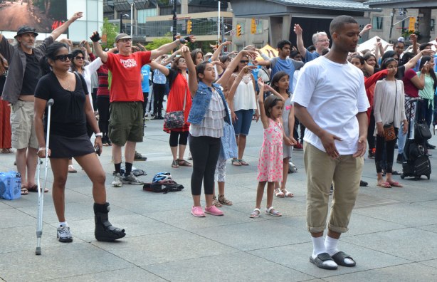 people dancing at Yonge Dundas Square as a group, part of an event called Sharing Dance - hands in the air