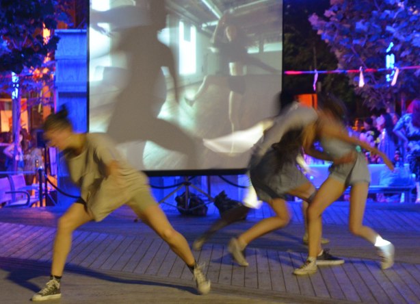 Dancers performing in front of a video playing on a screen, night time performance, some of the dancers are partly blurry