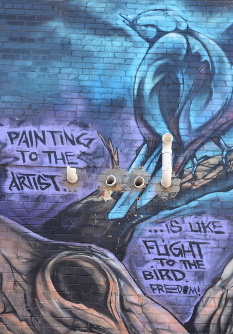 part of mural, a dark blue bird sits in a tree. The words "Painting to the artist is like flight to the bird. freedom"
