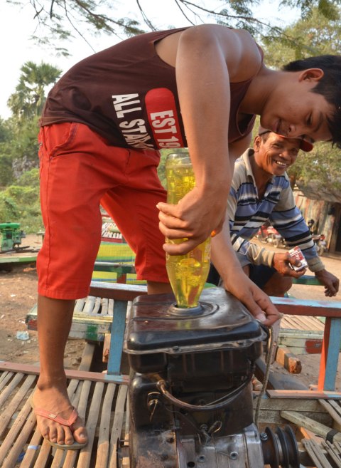 A boy fills an engine with yellow coloured gas that was in an old plastic pop bottle 
