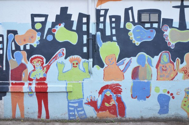 Part of a mural in an alley painted by students from Gledhill Public school, graduating class of 2009, black silhouette of the Toronto skyline with big colourful footprints, some roughly drawn people too
