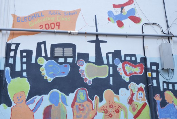 Part of a mural in an alley painted by students from Gledhill Public school, graduating class of 2009, black silhouette of the Toronto skyline with big colourful footprints, some roughly drawn people too , an airplane flies overhead