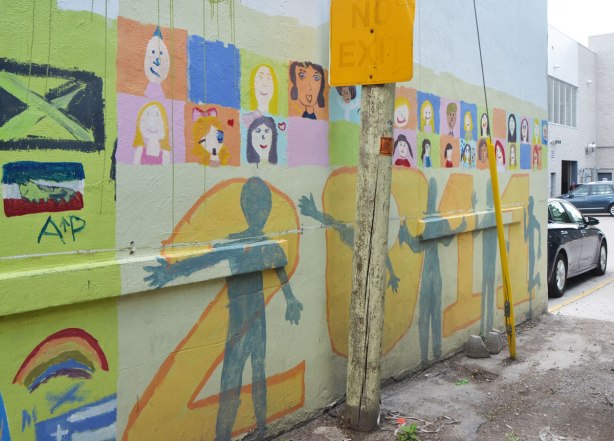 Part of a mural in an alley painted by students from Gledhill Public school, graduating class of 2011. 2011 in large numbers across the bottom with grey silhouettes of people, brightly coloured squares with faces across the top