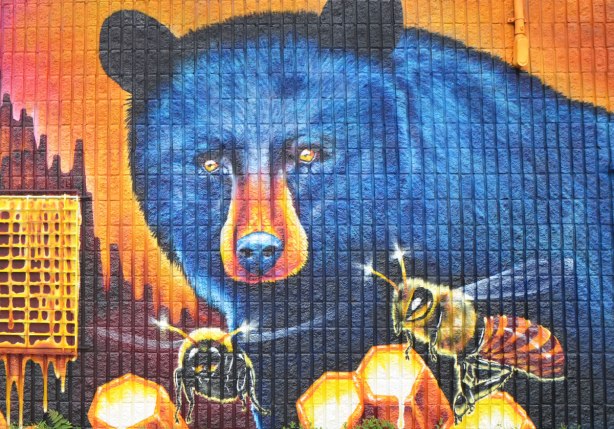 part of a large mural by Nick Sweetman on a wall in Frank Kovac Lane, two very large blue bears are eating honey from honeycombs while a few large bees buzz around - close up of one bear's face