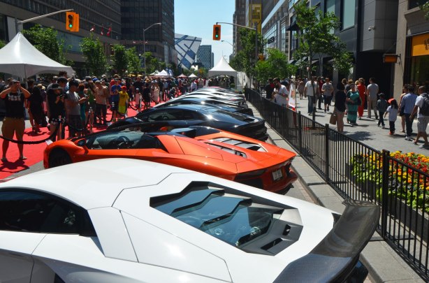 Several lamborghinis parked beside each other on Bloor Street as part of the Yorkville exotic car show. Lots of people are looking at them. 