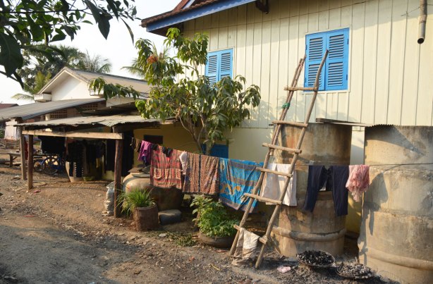 a light yellow house with blue shutters, a ladder made of poles leaning against the side of the house, laundry hanging on a rope beside the house