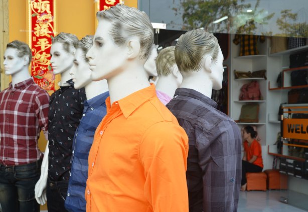 Two lines of white mannequins with black and white hair painted on, modelling men's shirts, in front of a store