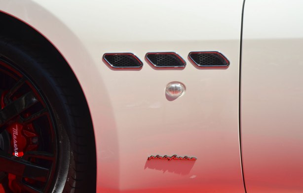 close up shot of the front side panel of a white Maserati Pininfarina car, reflections of a red carpet make the bottom part of the car look pink