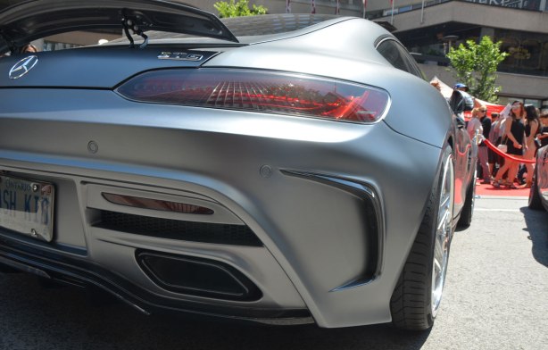 silver mercedes gts car, viewed from behind the back passenger side wheel, parked on Bloor St. for a car show. Some people in the background. 
