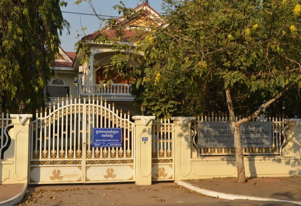 the exterior of the church of latter Day Saints (Mormons) behind a gate and trees in Cambodia. Looks like a house, yellow fence and gate