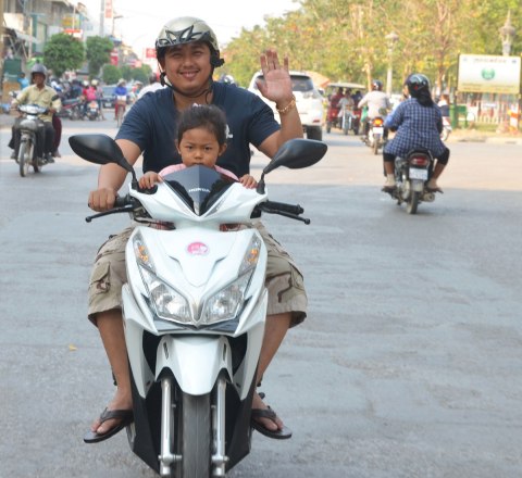 A father and daughter on a motorcycle. The girl is in front. The man is waving. 