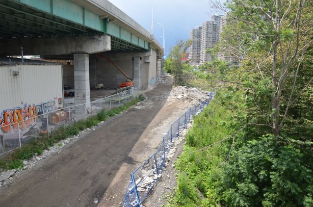 a dirt road runs alongside the Gardiner Expressway, some condos in the distance