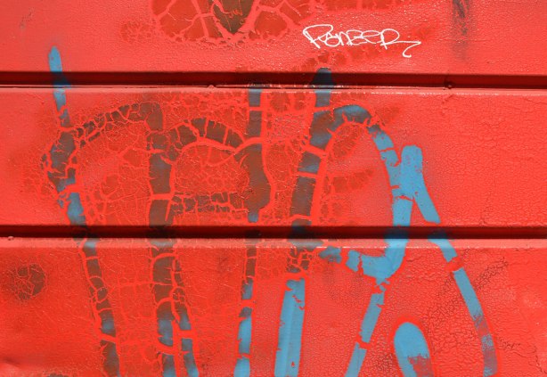 part of red garage with paint starting to peel where blue lines have been sprayed on. 