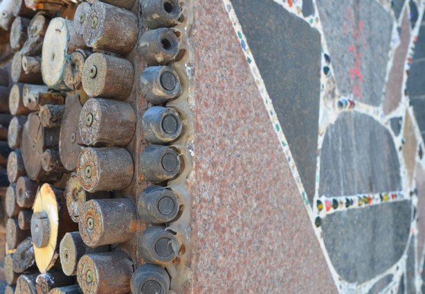 garage in a laneway decorated by Albino Carreira using slices of wood, pool cues, toy figures, and small found objects - an edge, pool cues pieces on one side, tips from pool cues down the center and flat slabs of polished stone with marbles on the other side 