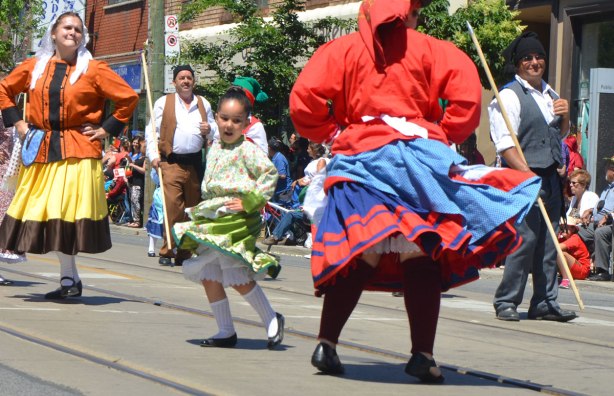 A young girl swirls her long skirt as she dances in a parade. Portugal Day parade on Dundas West, Little Portugal, in Toronto