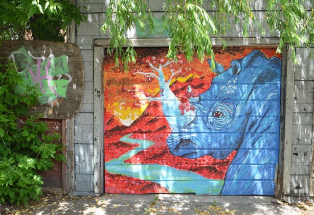 graffiti street art animals painted on garage door in an alleyway - a blue rhinoceros with a horn that looks like a tree