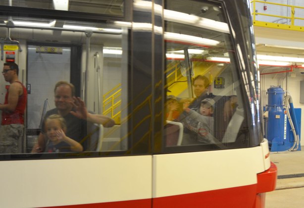 people riding in a new streetcar, photo taken from the outside, most of them are waving