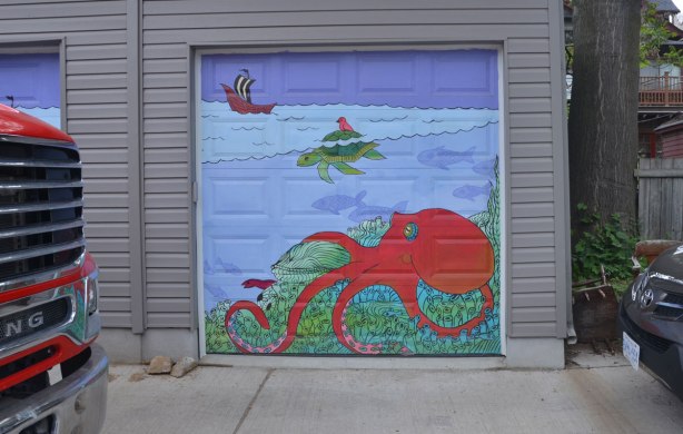marine scene street art on a garage door in a lane, a red octopus, a green turtle swimming and a ship in the distance