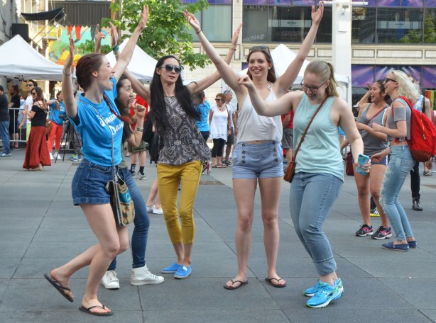 people dancing at Yonge Dundas Square as a group, part of an event called Sharing Dance - 5 young women with the arms in the air
