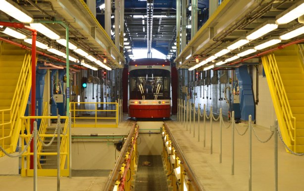the back of a new streetcar as it passes through interior of Leslie Barns streetcar facility, a large, tall interior space with lots of pipes 