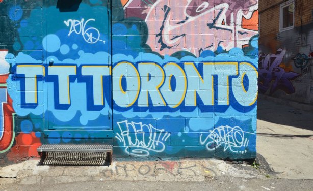 Street art painting in a n alley that says Toronto in blue