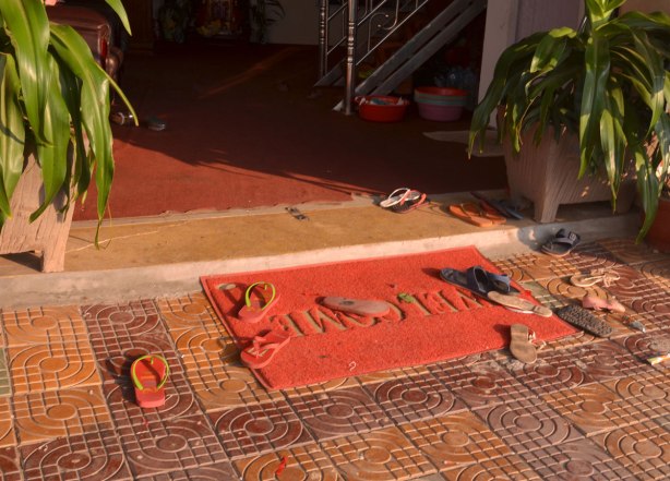 a large red welcome mat outside a store with many sandals and flip flops on it. 