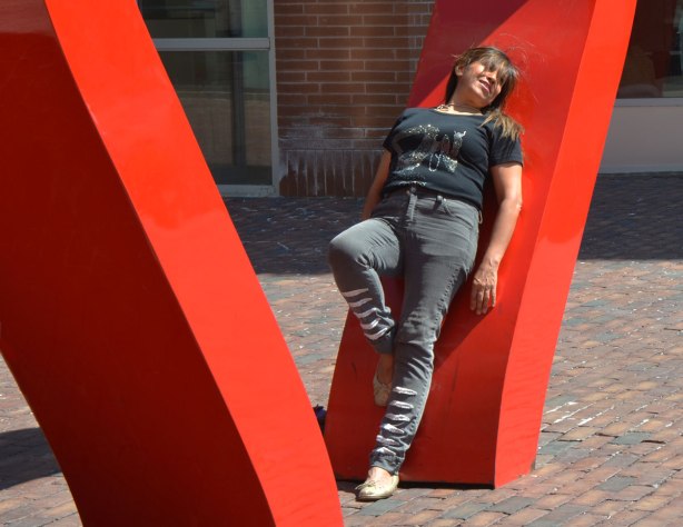 A woman is posing by the large red heart in the distillery district, she is leaning back on one side of it.