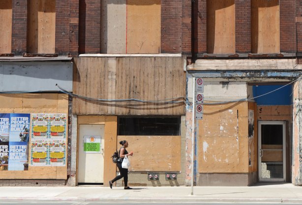 a woman walks on a sidewalk on Yonge St past old brick buildings with their doors and windows boarded up