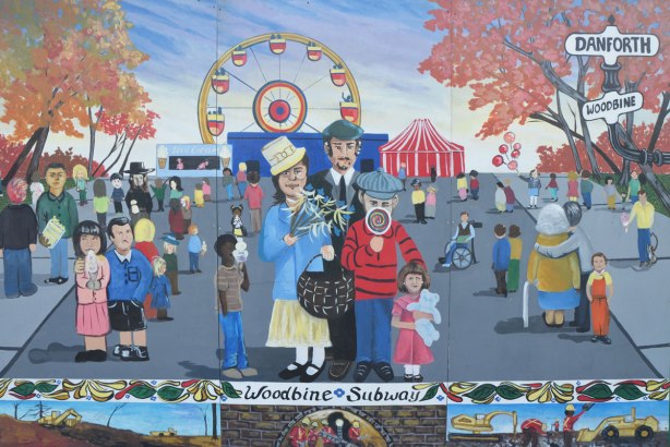 mural depicting people at a fair. A child is licking a giant round lollipop, a girl is holding a doll, a ferris wheel is in the background.