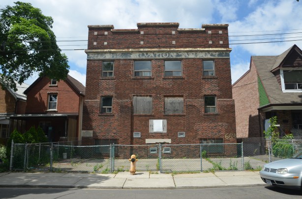 ghost sign, Salvation Army, across the top of an old brick building, number 668 Brock St., three storeys with fancy brickwork across the top of the roofline. boarded up, metal fence in front, concrete covered front yard, yellow fire hydrant.