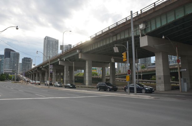 major road with traffic under an elevated expressway in a city, long ramp from the upper level to the lower. Gardiner Expressway and Lakeshore Blvd in Toronto, at Spadina looking west