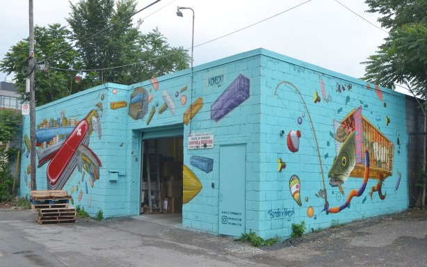 mural on two sides of a building in an alley, on turquoise, large swiss army knife, and a fish in a cage, reaching out with a long skinny arm, with a fishing rod