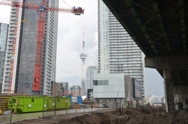 construction site under the Gardiner, cranes and condos being developed on the left, CN tower in the fog in the distance. 