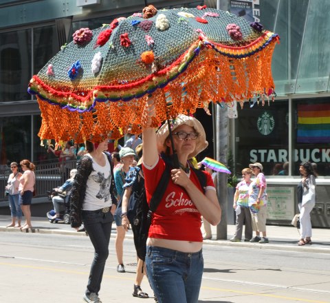 walkers in a dyke march in Toronto - a woman carries a large crocheted umbrella with a multicoloured fringe